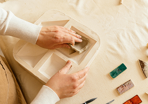 Une femme âgée souriante, sculptant un objet en argile dans un atelier collectif.